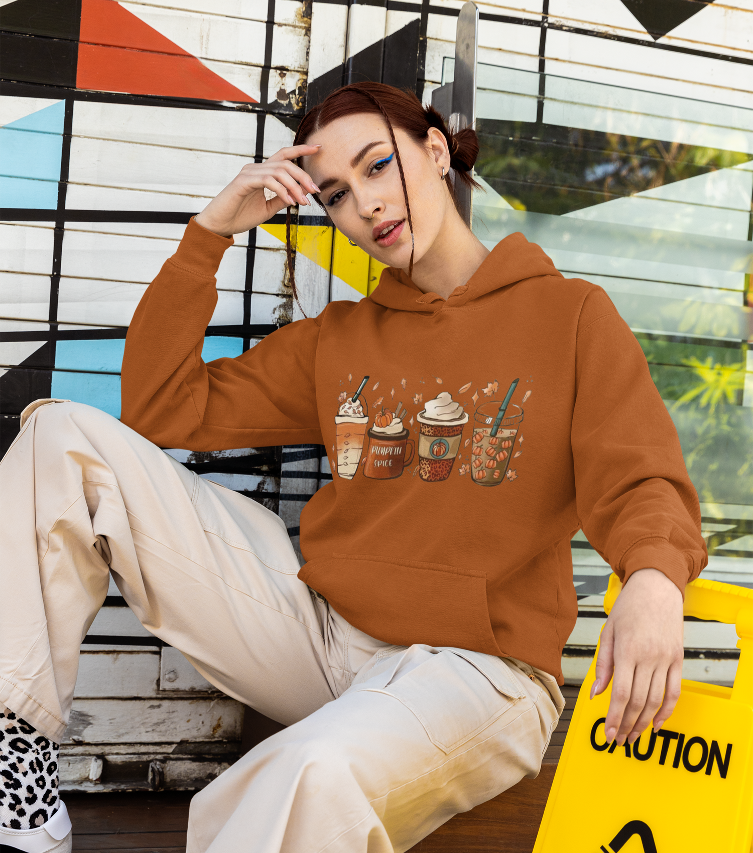 Person wearing a brown hoodie with graphic designs sitting on a bench.